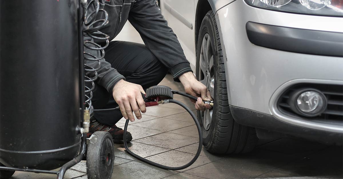 A person in black jacket and black pants checking a car's tire