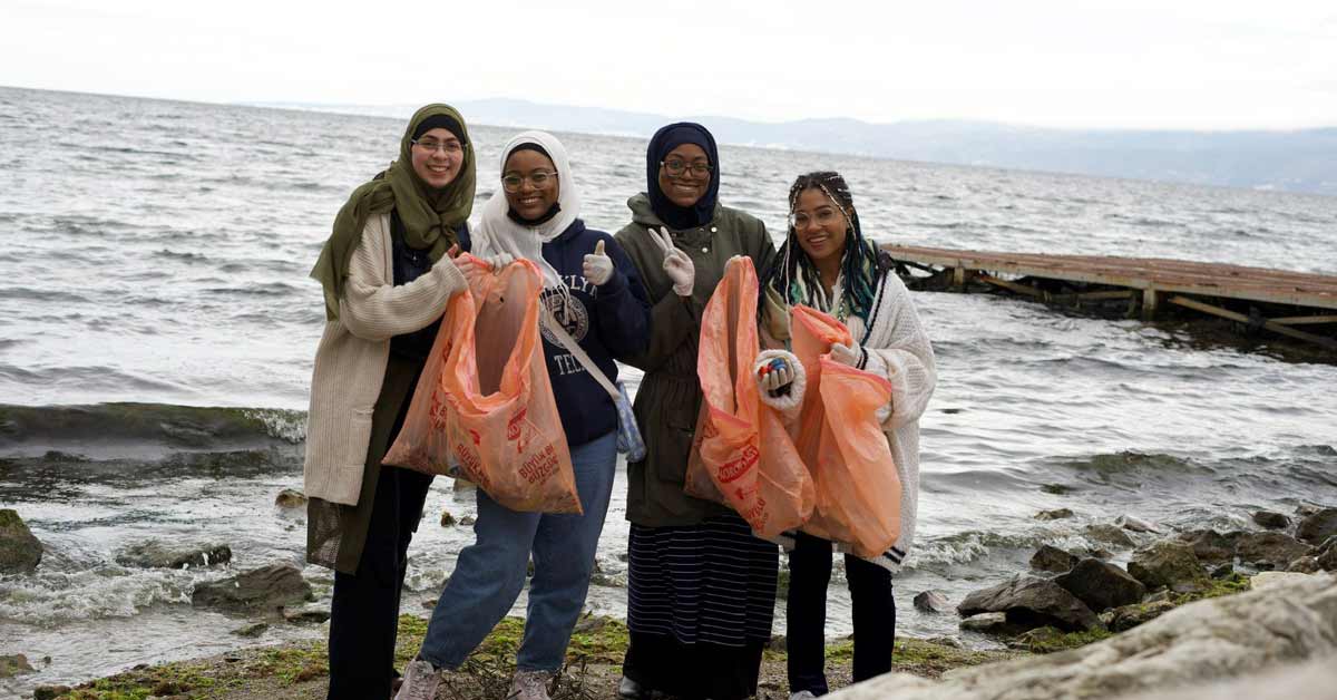 Four women smile, holding trash bags along a shoreline in Turkey