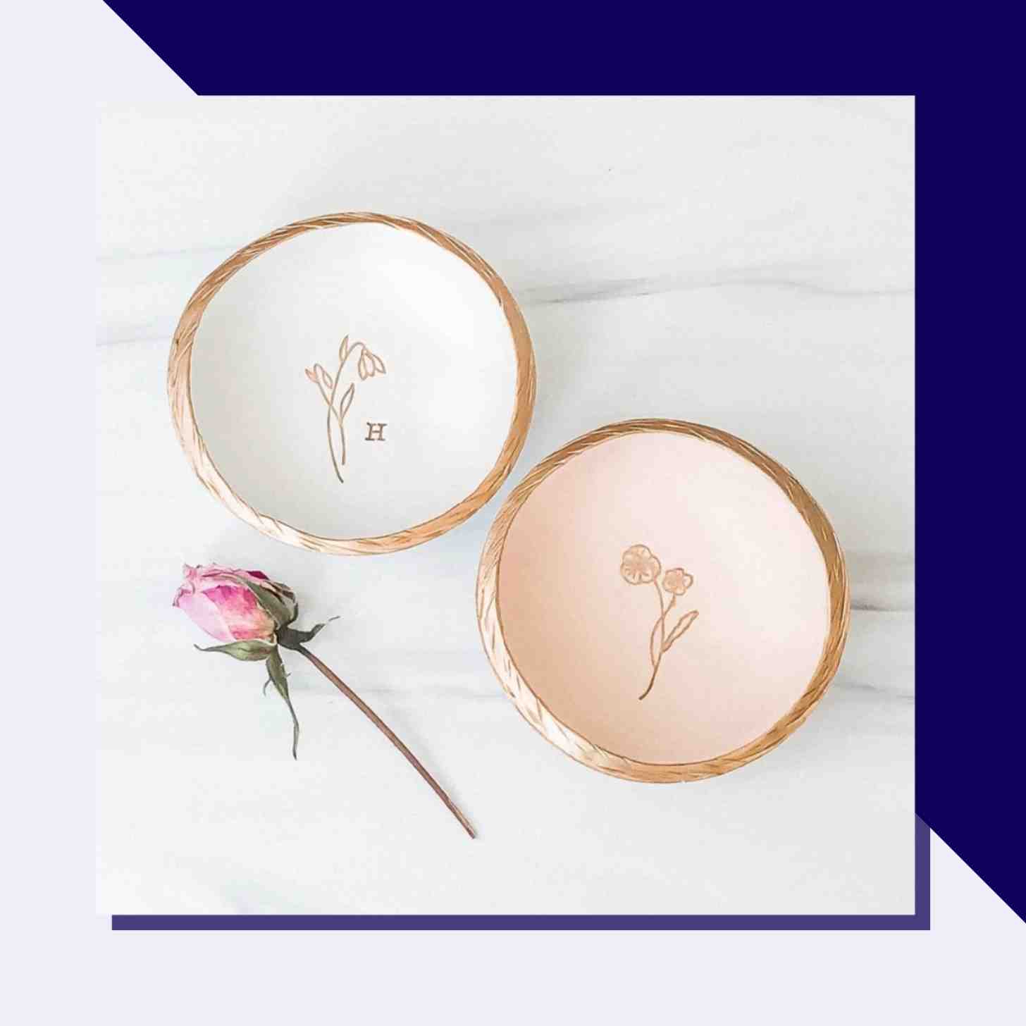 Two Jewerly Dishes With Engravings Inside Displayed On A Table With A Pink Rose