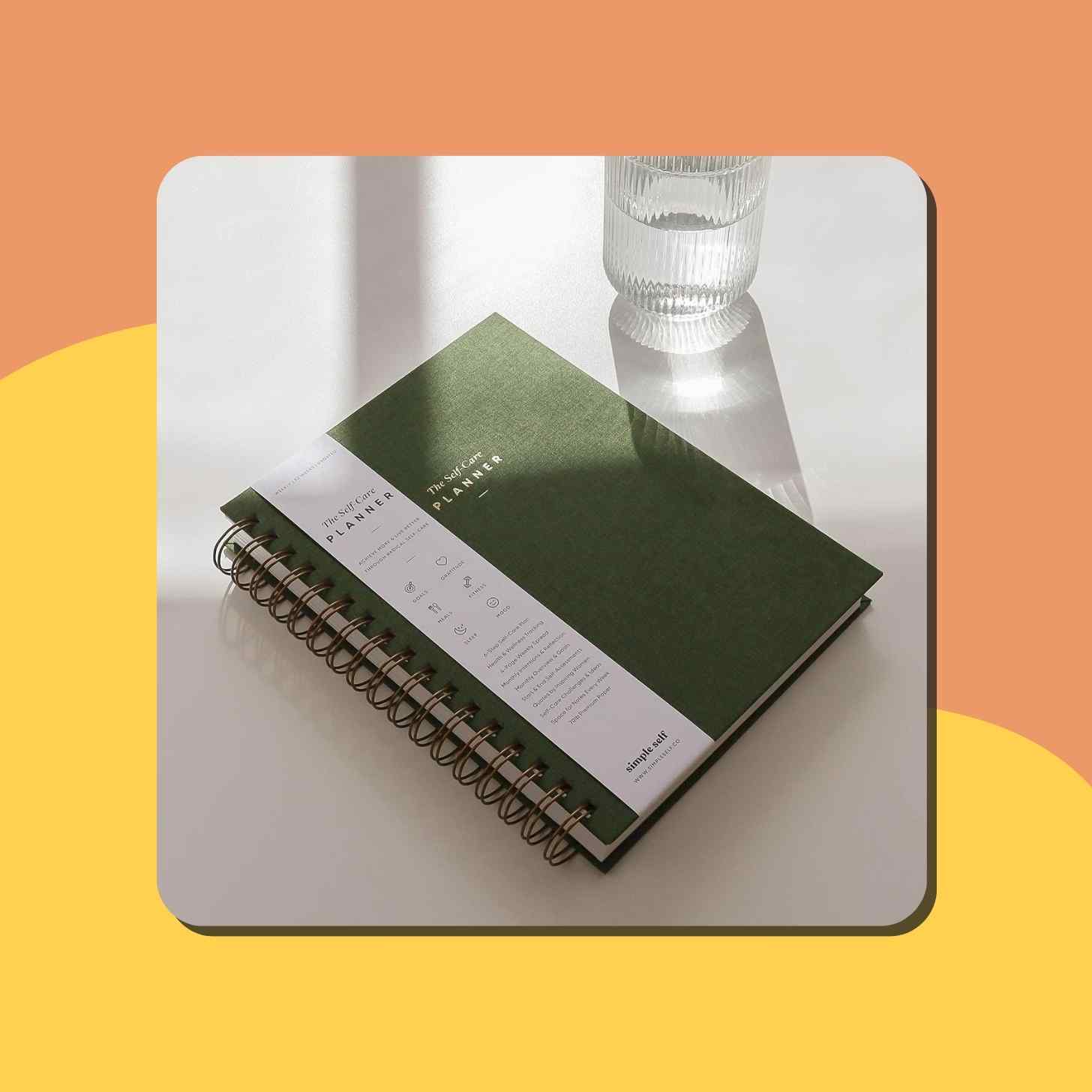 A Green Simple Self Care Planner On A Table Next To A Glass Of Water