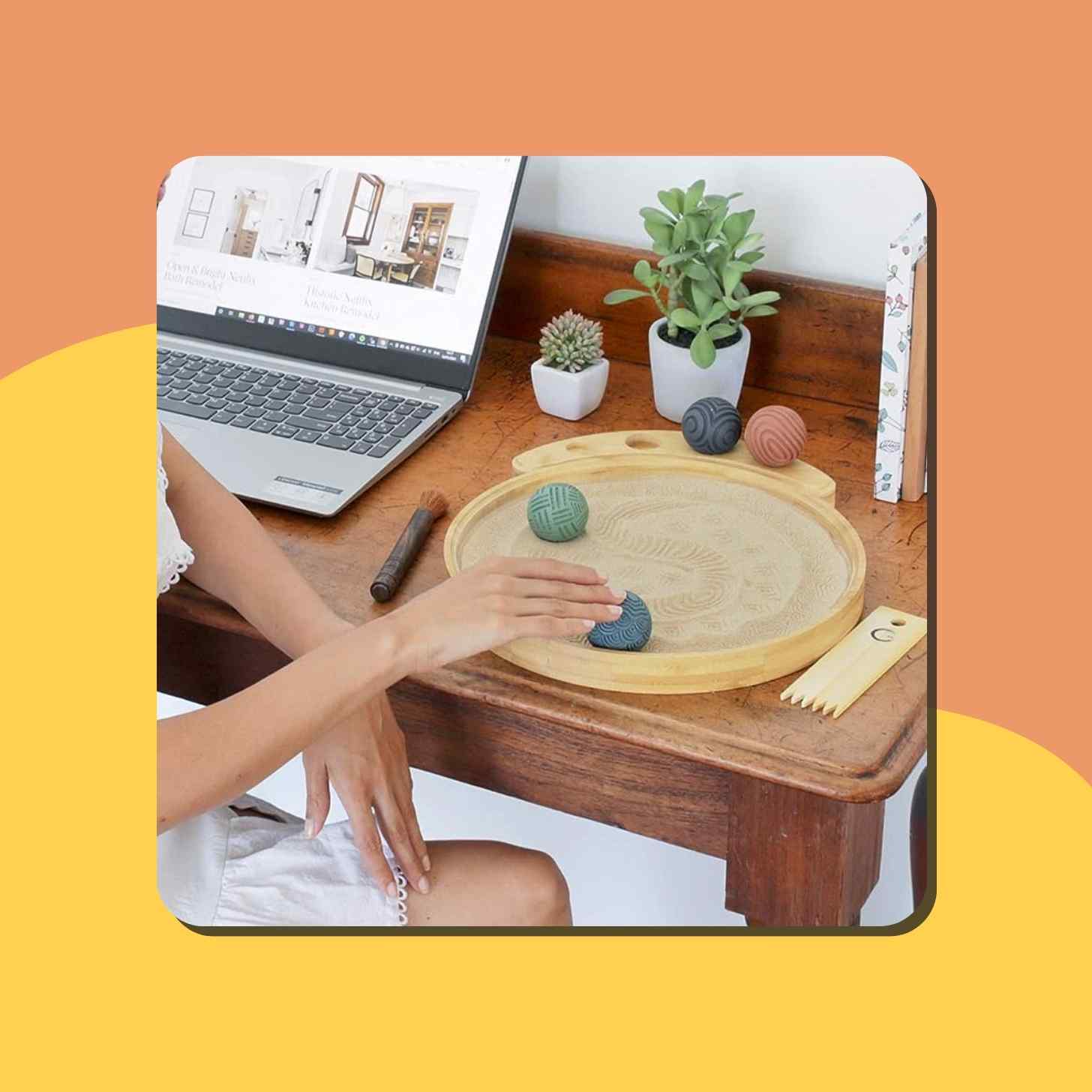 A Person Touching A Tabletop Zen Garden Next To Their Laptop Setup