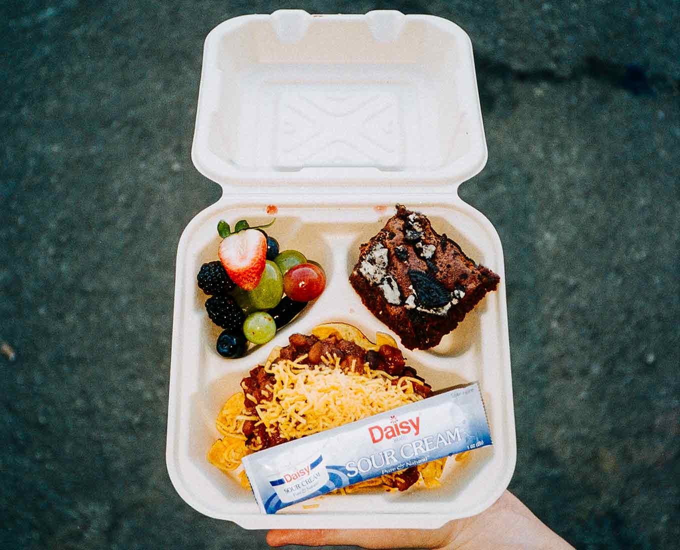 A to-go container is filled with tacos, fruit, and dessert.