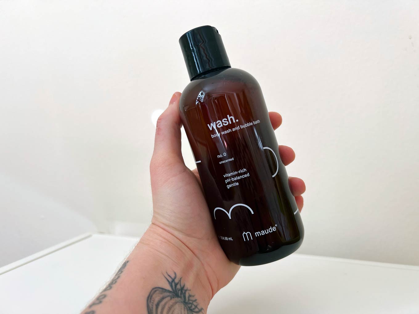 A hand holds up a bottle of Maude's body wash