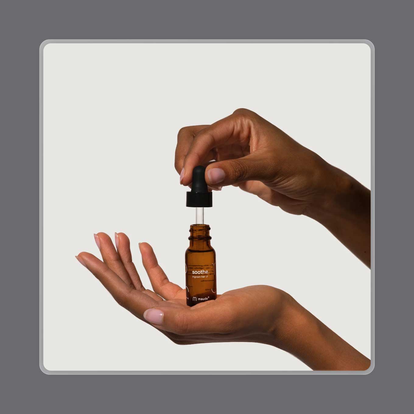 A hand holds up a dropper above an amber jar of ingrown hair oil