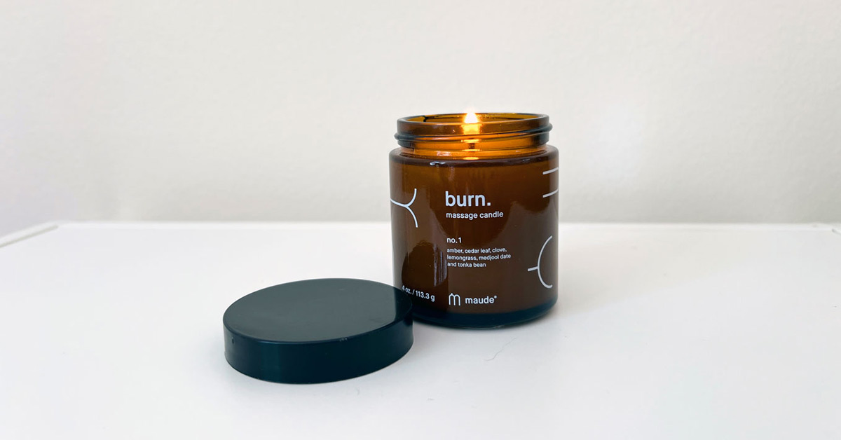 A lit massage candle in a small amber jar sits on a white countertop