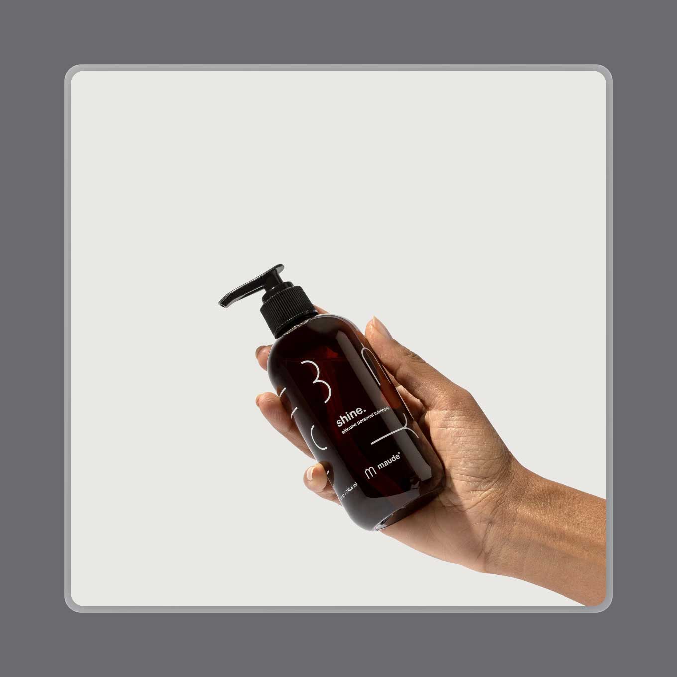A hand holds up a bottle of Maude's Shine Silicone lube