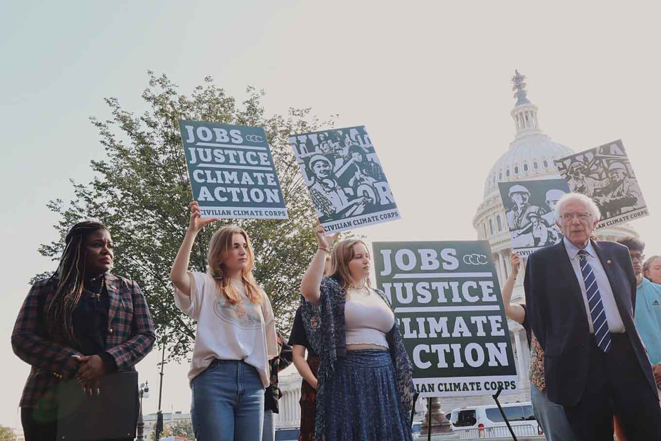 Activists hold signs at a rally that say "jobs, justice, climate action"