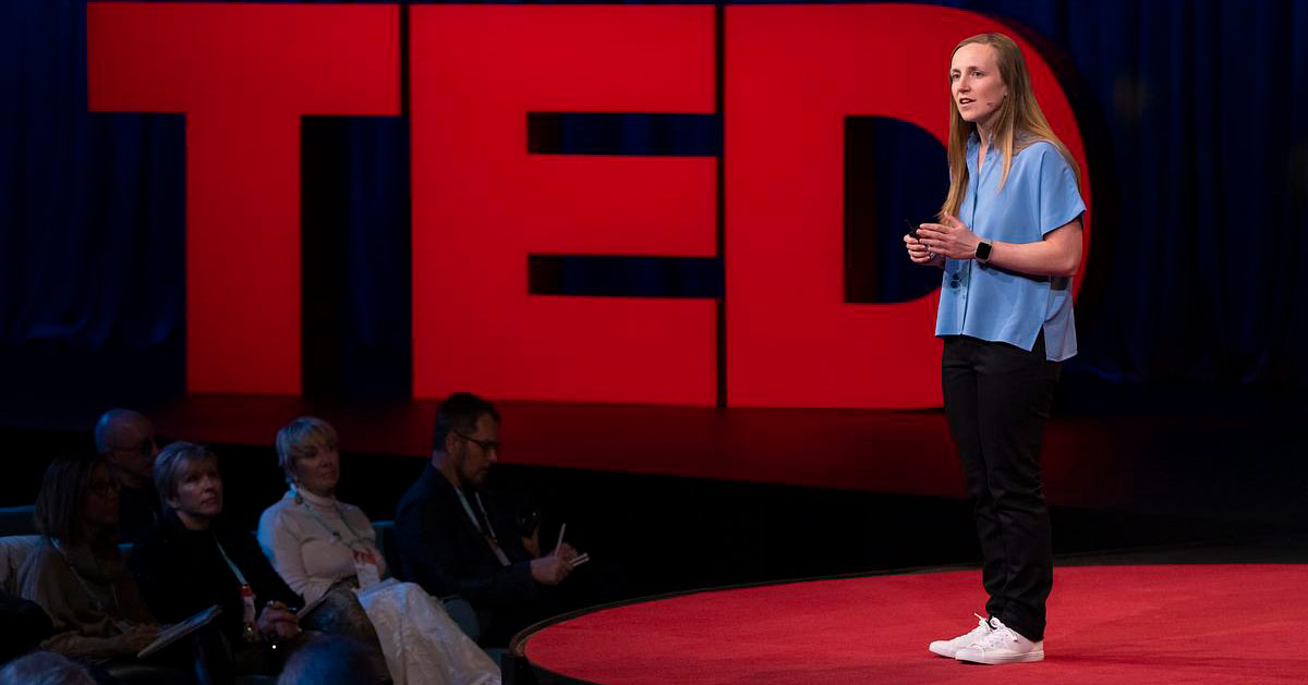 Hannah Ritchie stands on red stage in front of the red TED Talks logo